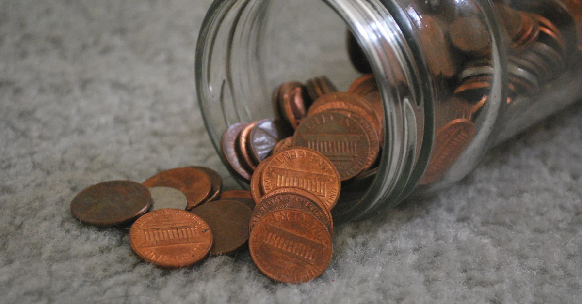 Pennies spilling out of a glass jar onto a table