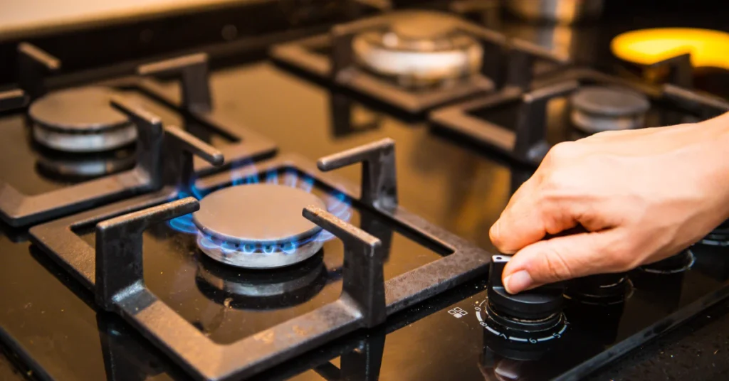 Hand turning the knob of a gas kitchen stove with a lit blue flame