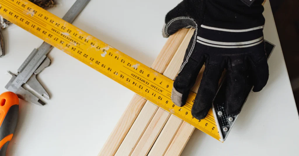 Gloved hand measuring a wooden board with a yellow ruler