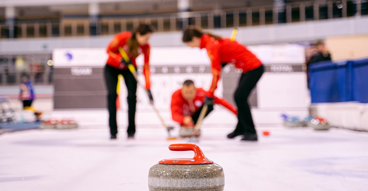 Curlers sweeping ahead of a sliding curling stone to show how much a curling stone weighs