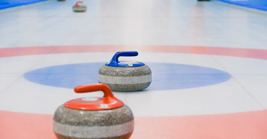 Red-handled Olympic curling stones resting on the ice near the house