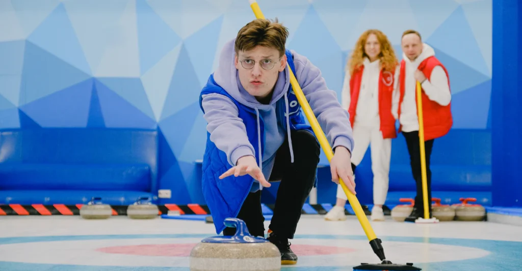 Curler delivering a granite curling stone across the ice while teammates watch