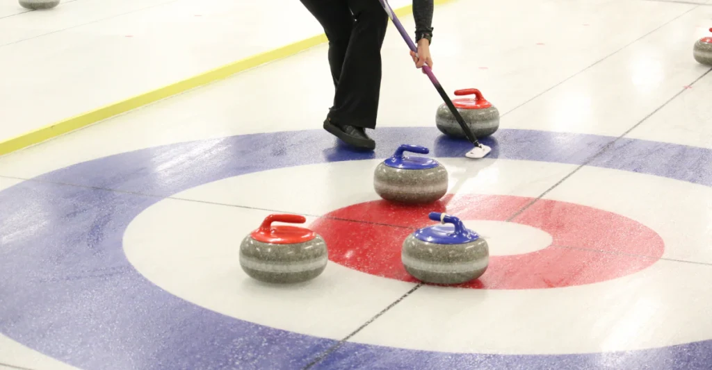 Curler sliding a stone toward the house while a teammate sweeps the ice