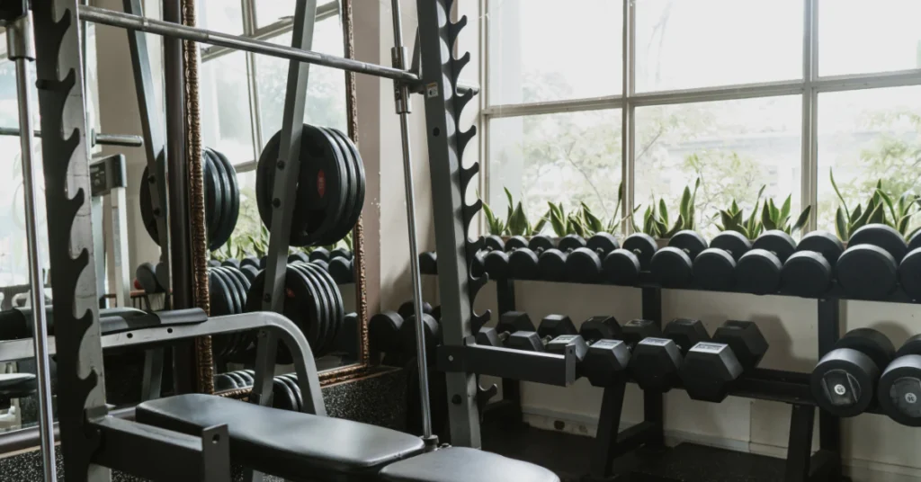 Empty Smith machine setup in a commercial gym with dumbbell rack in background