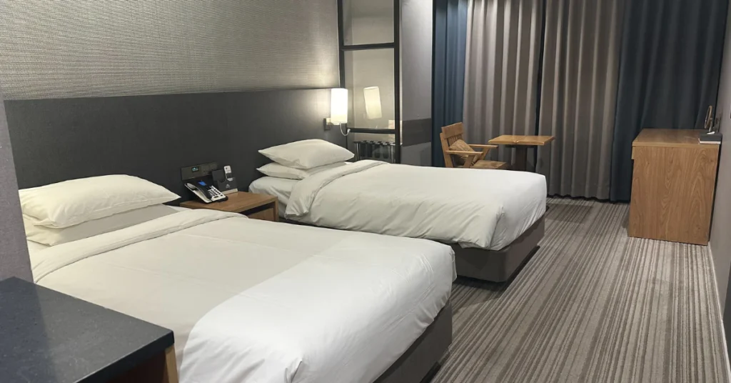 Bedroom with two single beds, white bedding and a wooden headboard wall