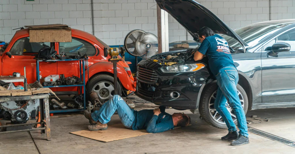 Mechanics working on a red car inside a large garage workshop