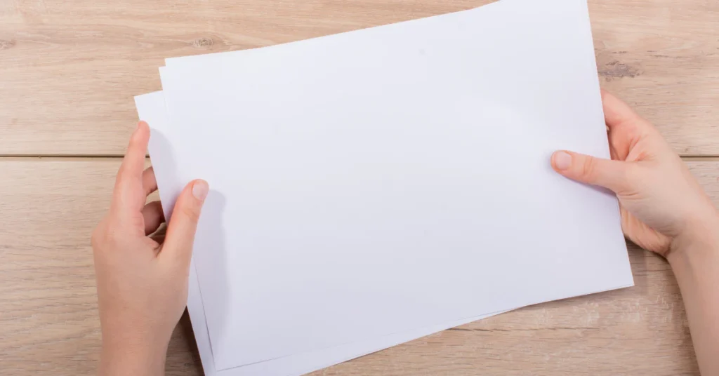 Hands holding a blank sheet of paper over a wooden table