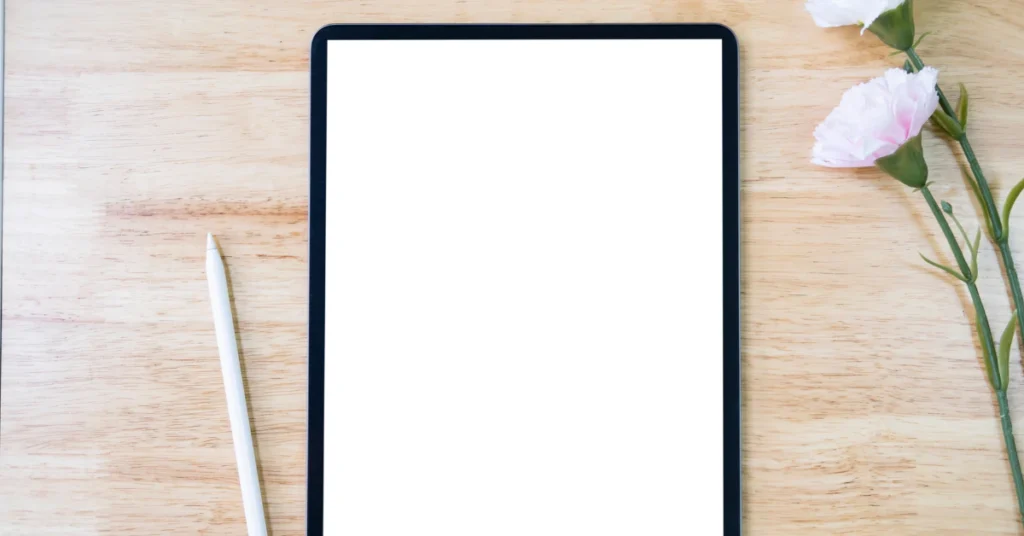 Tablet with a blank white screen lying on a wooden desk