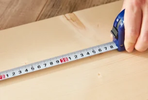 Hand pulling a measuring tape across a wooden surface to measure length