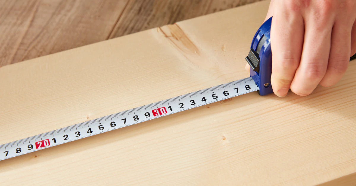 Hand pulling a measuring tape across a wooden surface to measure length