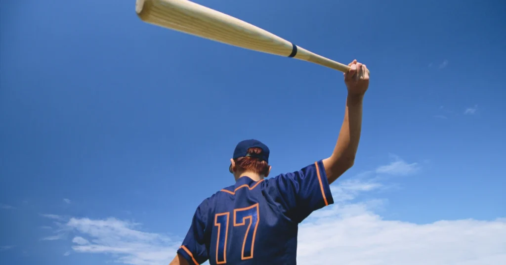 Baseball player holding a bat up against a blue sky