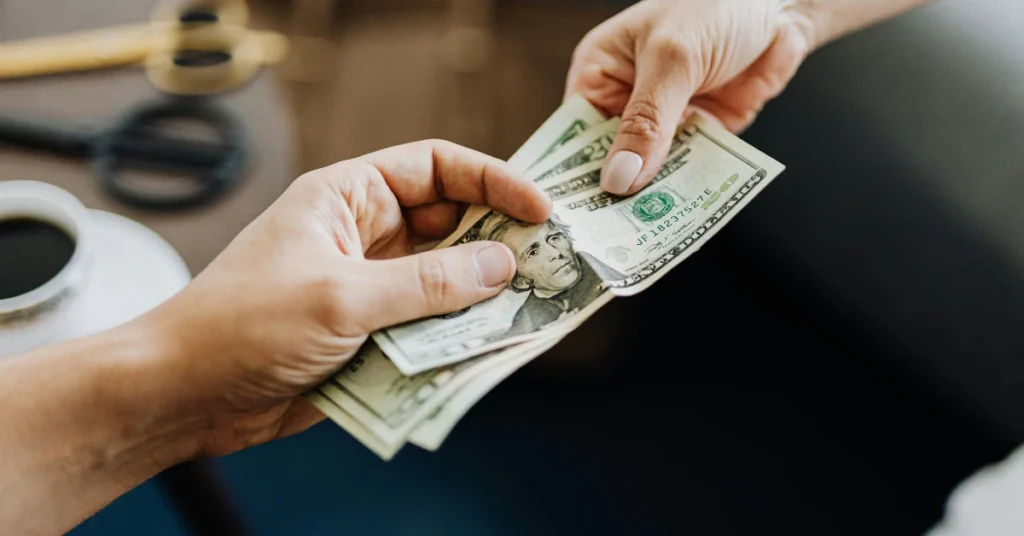 Hands counting US dollar bills, often wrongly used to estimate 9 inches