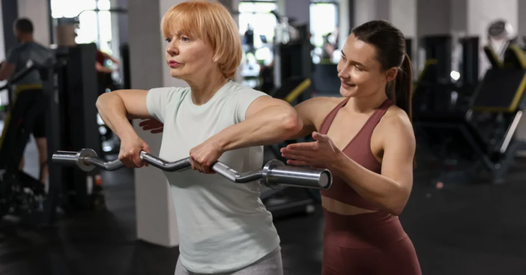 Trainer guiding a woman through a bar curl exercise in a gym
